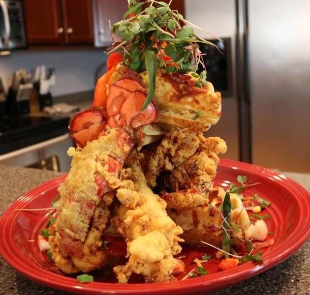 A stack of fried lobster and waffles on a red plate on a table in a kitchen.