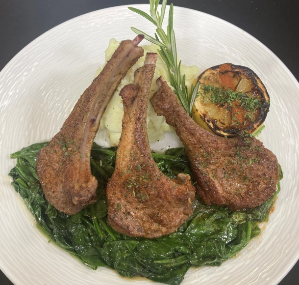 A plate of food with herb-crusted lamb chops, creamy polenta, and spinach